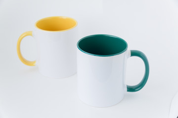 Two white mugs, with a green and yellow handle on a light background. 