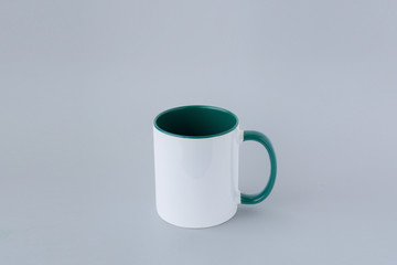White mug with a greeen handle on a gray background.