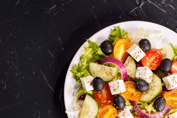 Greek salad with fresh vegetables, feta cheese and black olives on a dark stone slate background. Top view. Free space for your text.