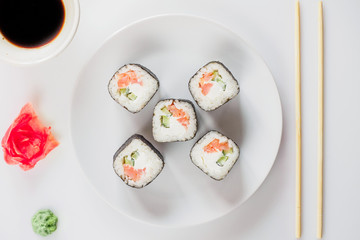 Japanese restaurant, sushi roll on white plate. Set for one person with chopsticks, ginger, soy, top view, copy space