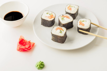 Japanese restaurant, sushi roll on white plate. Set for one person with chopsticks, ginger, soy, top view, copy space