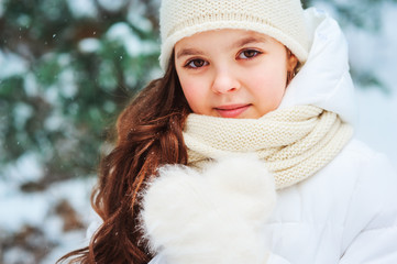 Winter close up portrait of cute dreamy child girl in white coat, hat and mittens playing outdoor in snowy winter forest. Traveling, vacation and active winter holidays concept