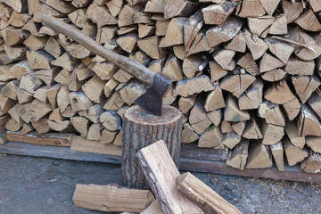 Dry oak firewood stacked in a pile, chopped wood for winter heating of the fireplace. An ax and a deck for chopping wood. Natural wood background.