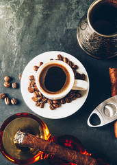 Cup of coffee, coffee beans, ashtray with cigar on dark background