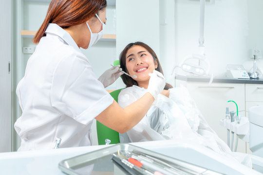 Healthy smile and a dentist. Smiling female patient sitting in the dental chair and smiling to dentist, dentist puts dental instruments to her face