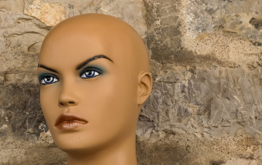 Close up of a vintage worn and distressed bald head of a plastic mannequin on public footpath, stone wall behind. Petrovac, Montenegro, - 227906340