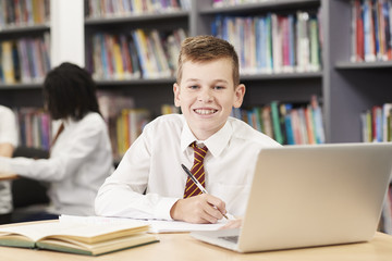 Portrait Of Male High School Student Wearing Uniform Working At Laptop In Library