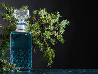 Blue gin in crystal decanter and juniper branch with berries.