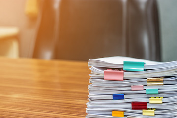 Stack of student's homework that assigned to students to be completed outside class on teacher's desk separated by colored paper clips. Document stacks arranged by various colored paper clips on desk.