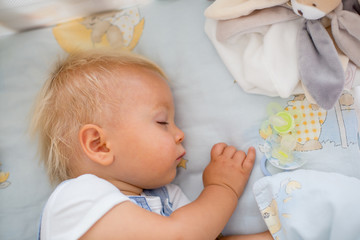 Little baby boy, sleeps in baby bed with pacifier and toys