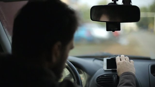 A man gets into the car and turns on the navigator on the smartphone, soft focus