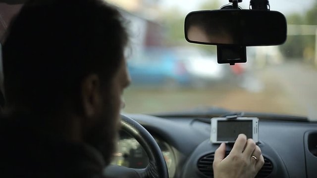 A man gets into the car and turns on the navigator on the smartphone, soft focus