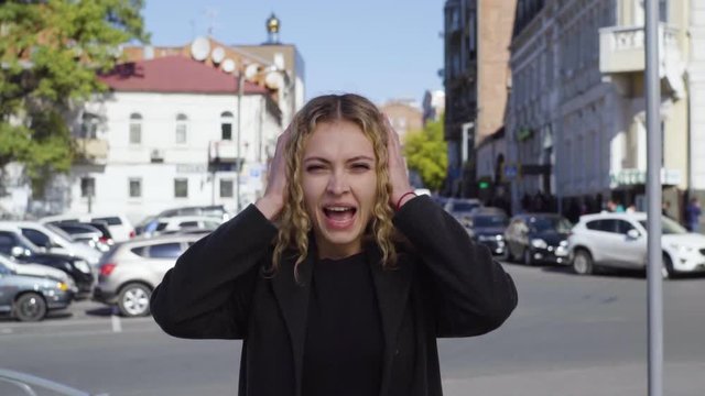 Screaming blonde woman covering her ears with closed eyes in the street of city