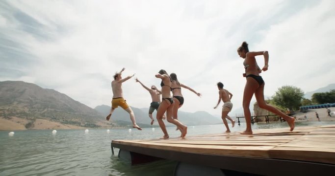 Group of young friends jumping from pier into lake, enjoying their holiday, having fun 4k