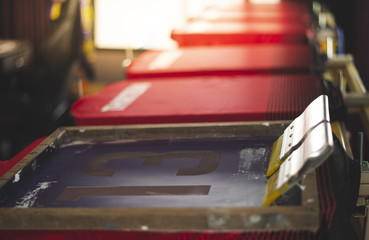 Red t-shirt screen printing, worker working on manual screen printing on t-shirt.
