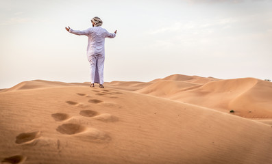 Arabic man with traditional emirates clothes walking in the desert
