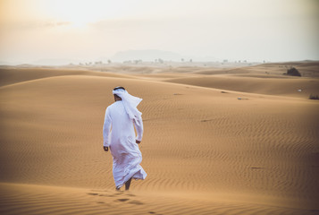 Naklejka premium Arabski mężczyzna chodzący po pustyni z tradycyjnymi ubraniami emiratów