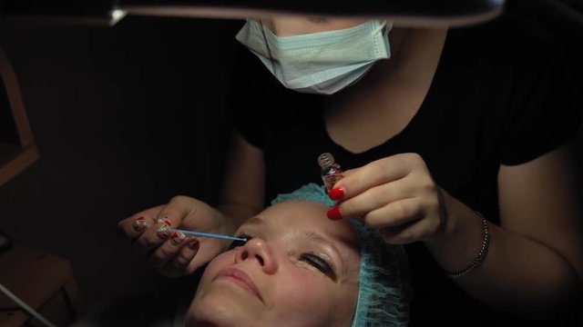 Makeup artist doing curling and keratin lash lift for female client, procedure for the care of eyelashes in a beauty salon, dolly shot.