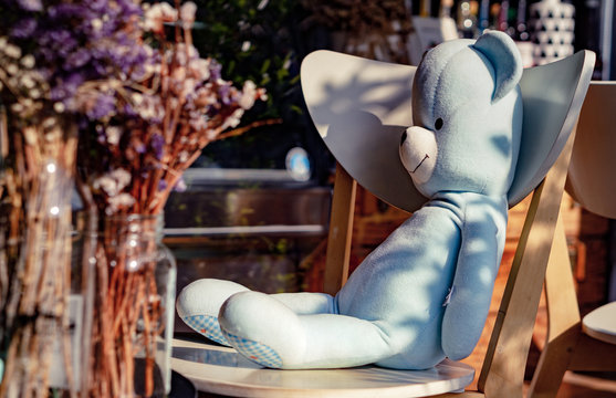 Lovely blue teddy bear toy sitting on the chair in bakery coffee shop.Concept about relaxing time with happiness. Home decoration creative idea .