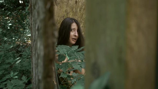 afraid and scared young woman hides in the forest