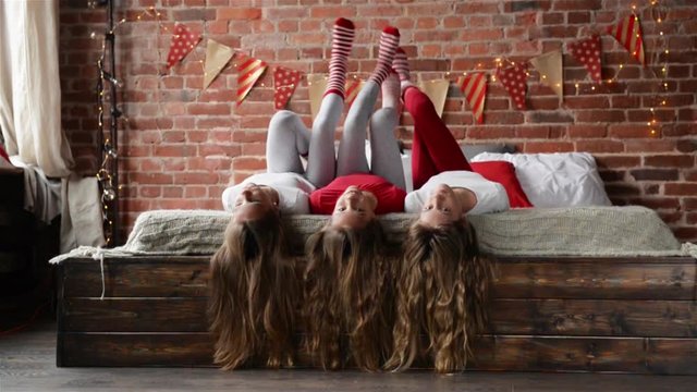 Three Sisters Lie on the Bed. Triplets Playing with her Long Hair in the Bedroom Decorated for Christmas. Merry Christmas and a Happy New Year.