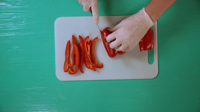 man wearing white gloves cutting fruit into slices. plant is red and juicy.