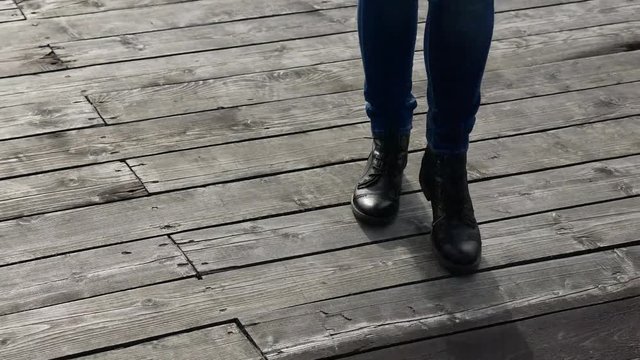 women's legs in blue jeans in black autumn shoes are on the wooden flooring on the street