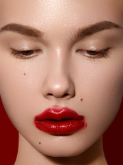 Cosmetics, makeup and trends. Bright lip gloss and lipstick on lips. Closeup of beautiful female mouth with red lip makeup. Beautiful part of female face. Perfect clean skin in red light