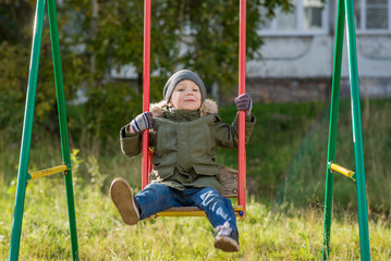 boy on a swing in a hat and a green jacket