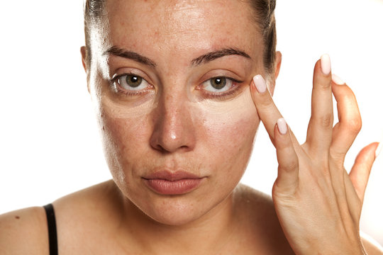 Young woman applying concealer under her eyes with her fingers on white background