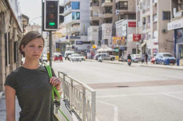 A young woman with a bag is standing at a crossroads at a traffic light