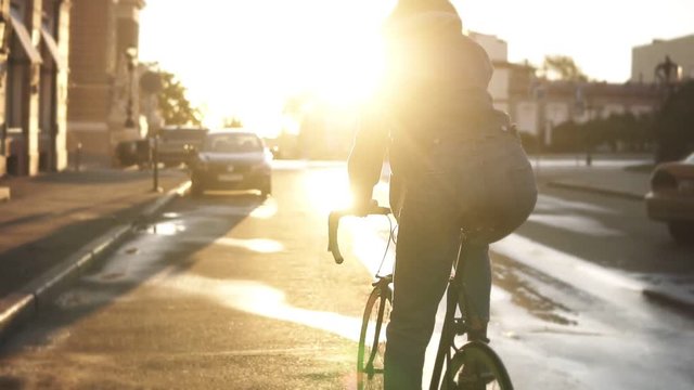 Rare view of a pretty caucasian female riding a bicycle in the morning empty street of a beautiful empty city. Young woman riding a trekking bike, wearing sneakers and casual clothes. Sun stronly