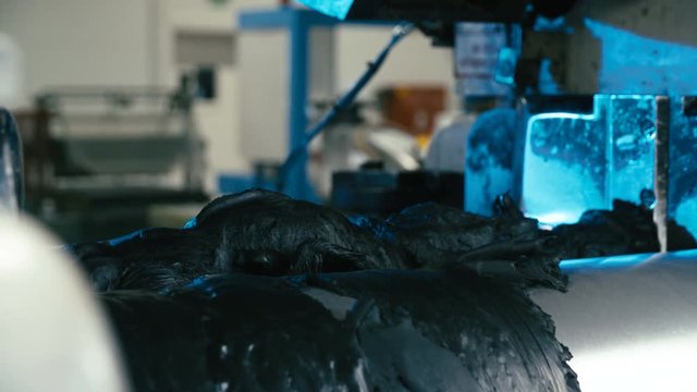 Raw rubber materials spin on industrial mixing cylinder 4K. Long shot of mixed rubber mass in focus while being rolled into cylinder machine. Industrial rubber production line.