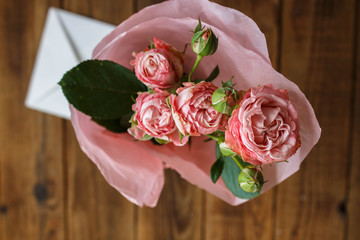 a bouquet of roses in a vase with envelope on wooden background