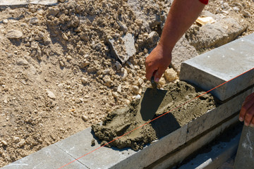 Masonry worker make concrete wall by cement brick and plaster at construction site, a spatula in the hands