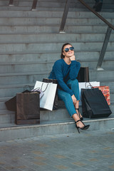 Beautiful girl with paper bags sits on a stairs outside shopping mall