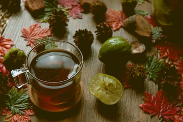 Autumn hot tea with lemon and spices in glass cup.on rustic table with leaves and pumpkins. Autumn Halloween style.