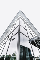 The corner of a modern business skyscraper with security video camera on the side; a contemporary office high-rise with surveillance video cam, glass facade reflecting the sky and surroundings