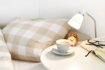 morning coffee on the bedside table, plus an alarm clock, lamp and book with glasses, lazy day...