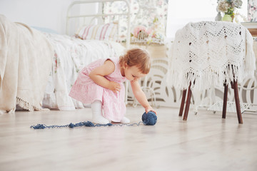 Childhood concept. Baby girl in cute dress play with colored thread. White vintage childroom