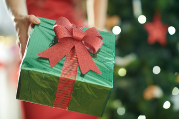 Christmas present box in a hand of woman near Christmas tree