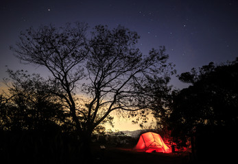 Fototapeta na wymiar Tent glows red against distant glow from city and starry night sky