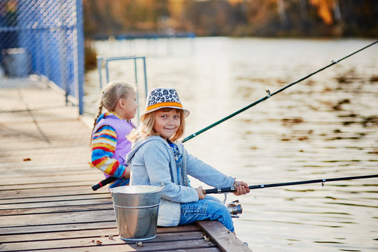 Little girls fishing on the lake, sitting on a wooden pontoon