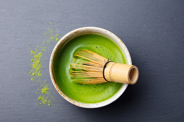 Matcha green tea cooking process in a bowl with bamboo whisk. Black slate background. Top view. - obrazy, fototapety, plakaty