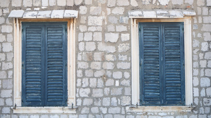 Two windows in old wall with closed blue shutters