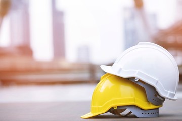 yellow and white hard safety wear helmet hat in the project at construction site building on concrete floor on city with sunlight. helmet for workman as engineer or worker. concept safety first.  - obrazy, fototapety, plakaty