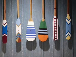 Wooden canoe Boat paddles with different color and shape of blades Hanging on a blue wood...
