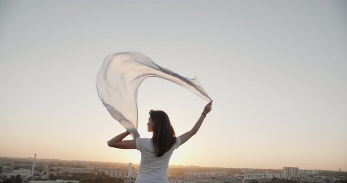 Young pretty girl standing on the rooftop, holding up her shawl in wind closeup 4k