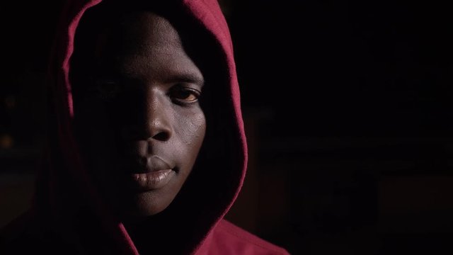 Hooded young black african man in the darkness staring at camera