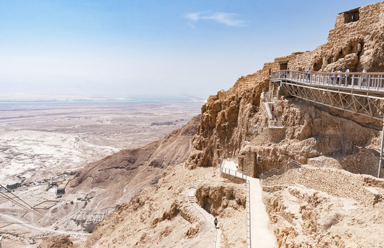 tourists at the main entrance of the ancient Masada fortress showing the upper part of the snake path and the cable car overlooking the Dead Sea
